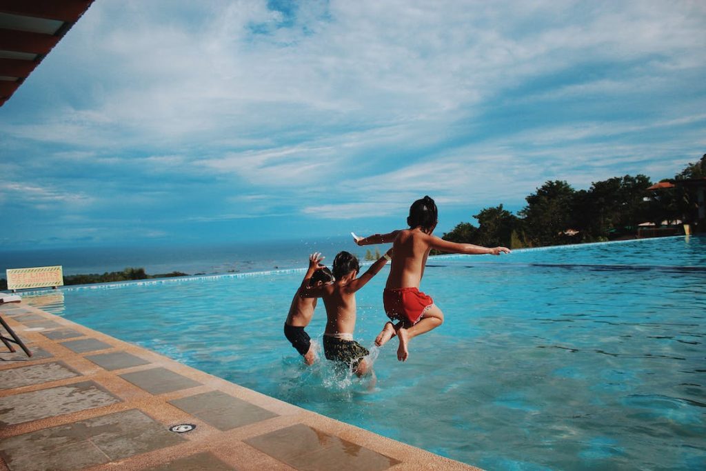 three teen swimmers jumping into a swimming pool