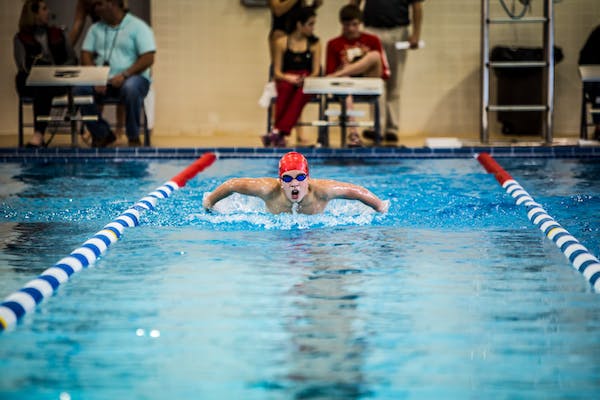 male swimmer with red swim cap preparing his body before swimming 100 yards