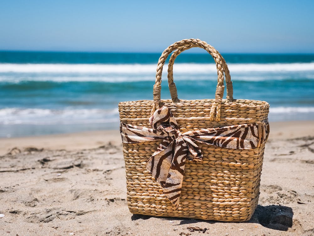 a brown woven beach bag placed beside the beach