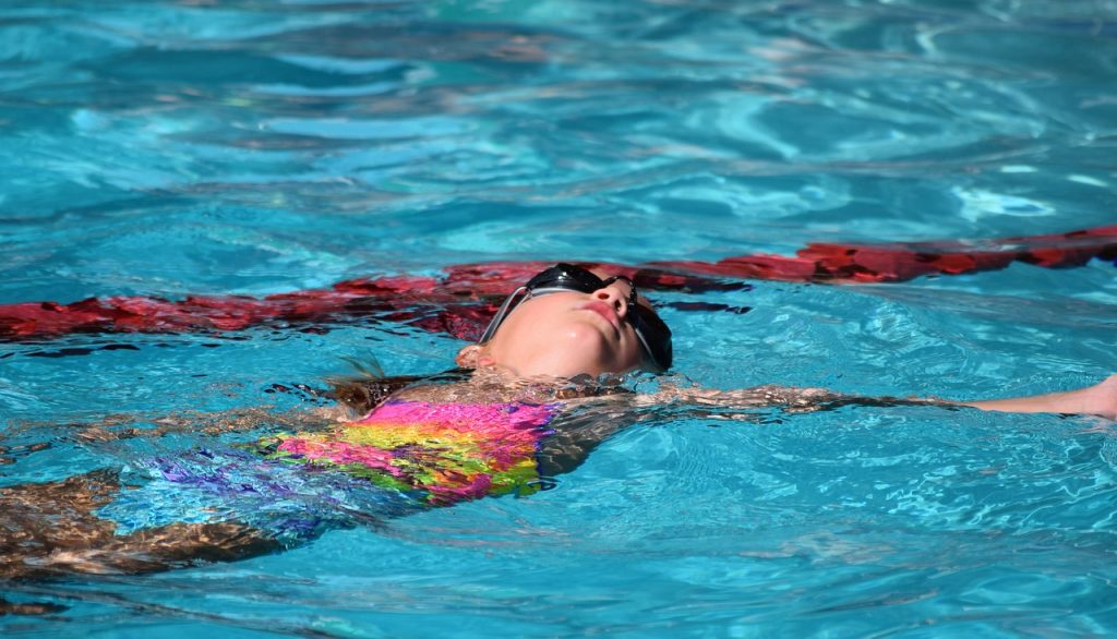 female young swimmer practicing the backstroke in a swimming pool